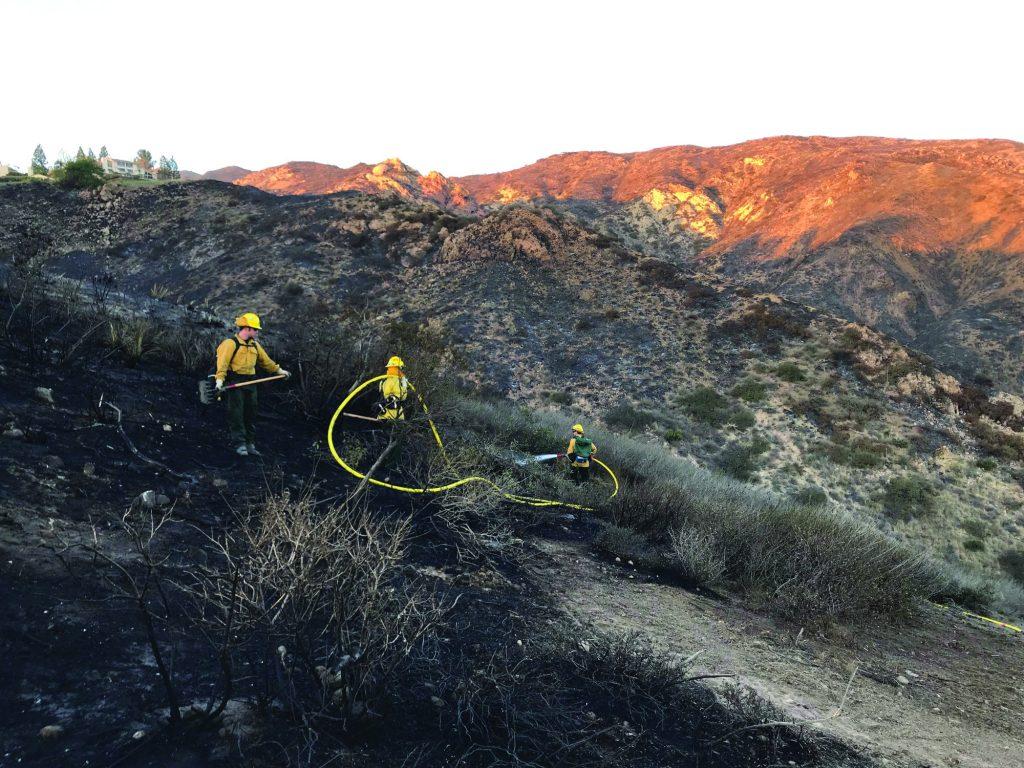 Firefighters carry equipment through the destructive Woolsey Fire aftermath in 2018.