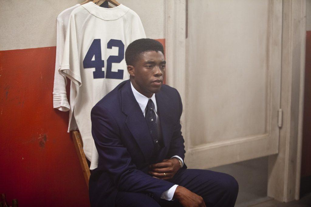 Robinson sits alone on a locker room bench in front of his official Dodgers jersey. Unlike his teammates who had lockers, he only had a hook in the corner.
