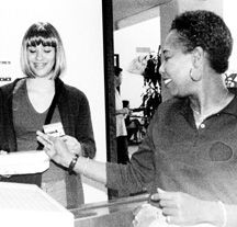 Cindy Cordner (right) hands a wig-wearing Vanessa Martinez her ID card. Photo/Lindsey Baguio