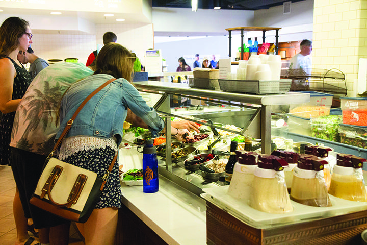 Students reach for toppings at the then-self-serve salad bar. Stations and bars that were self-serve are no longer permitted in the cafeterias across campus. File photo
