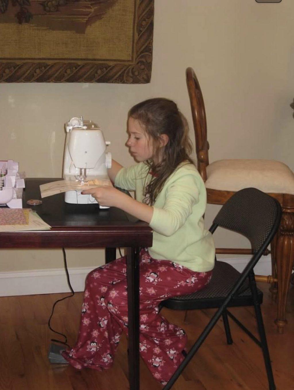 Murphy sits at a table with her first sewing machine, which she got when she was a child. She has been sewing for at least 10 years.