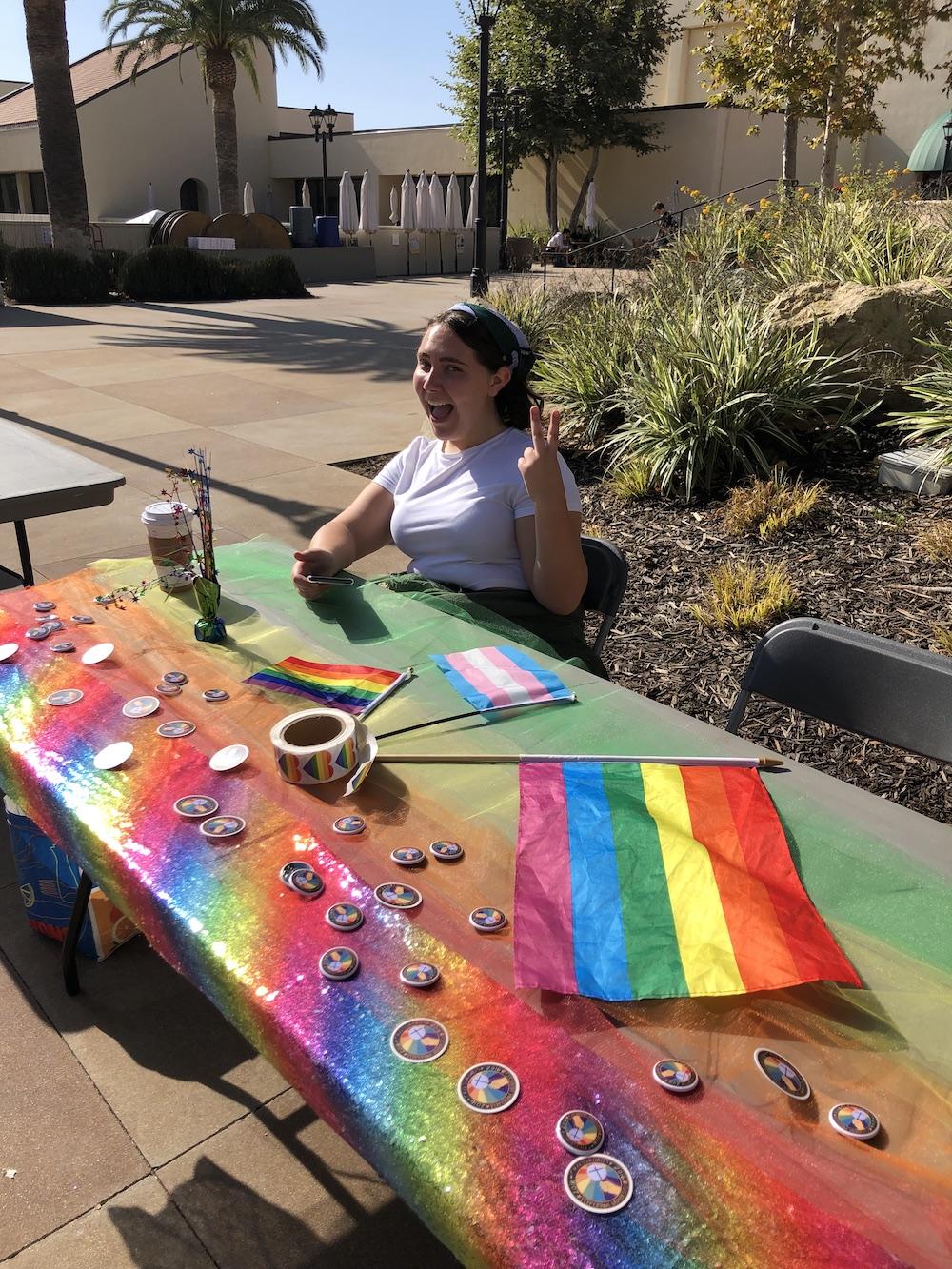 Buffaloe holds up the peace sign in 2019 at a booth for Crossroads Gender and Sexuality Alliance. She said she has made a lot of great connections through the club and hopes to continue mentoring children.