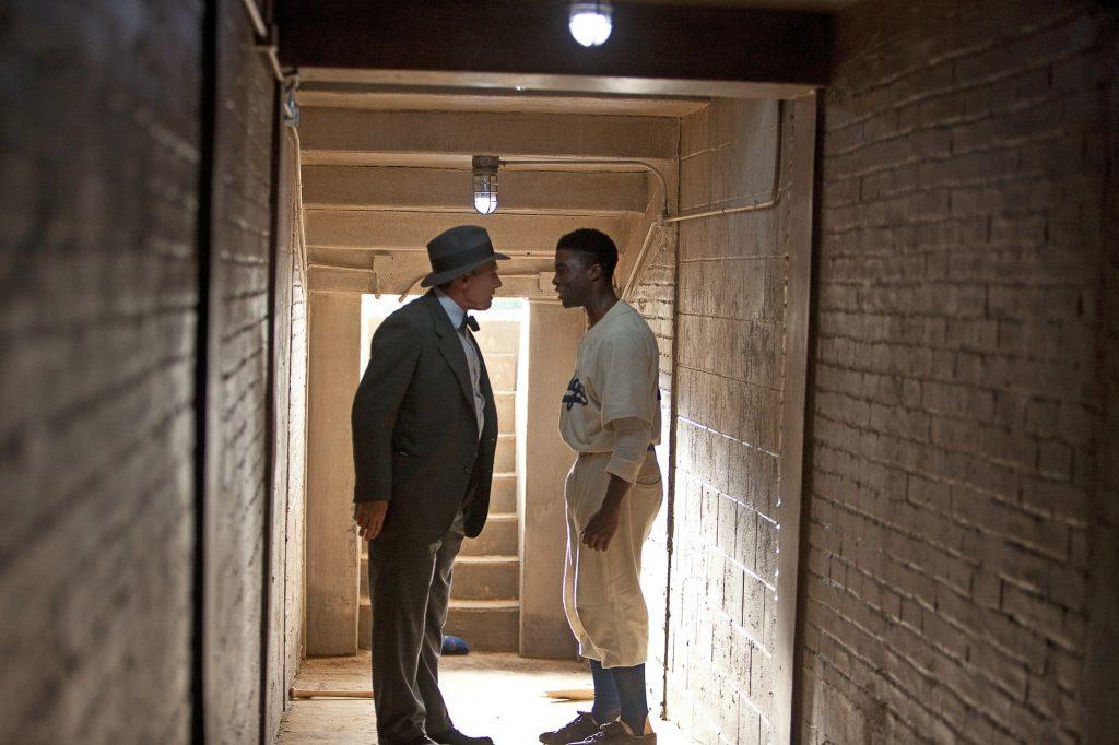 Dodgers owner Branch Rickey (Harrison Ford, left) encourages Robinson after Philadelphia coach Ben Chapman (Alan Tudyk) racially and publicly insulted Robinson off the field. Rickey wanted Robinson to believe in himself because the team counted on Robinson's performance to win.