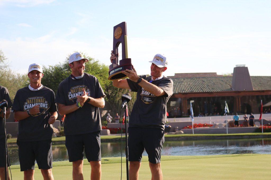Pepperdine Head Coach Michael Beard raises the trophy high on the 18th green. Beard is in his ninth season as the Waves' head coach, and this is his first national championship and the second in program history.