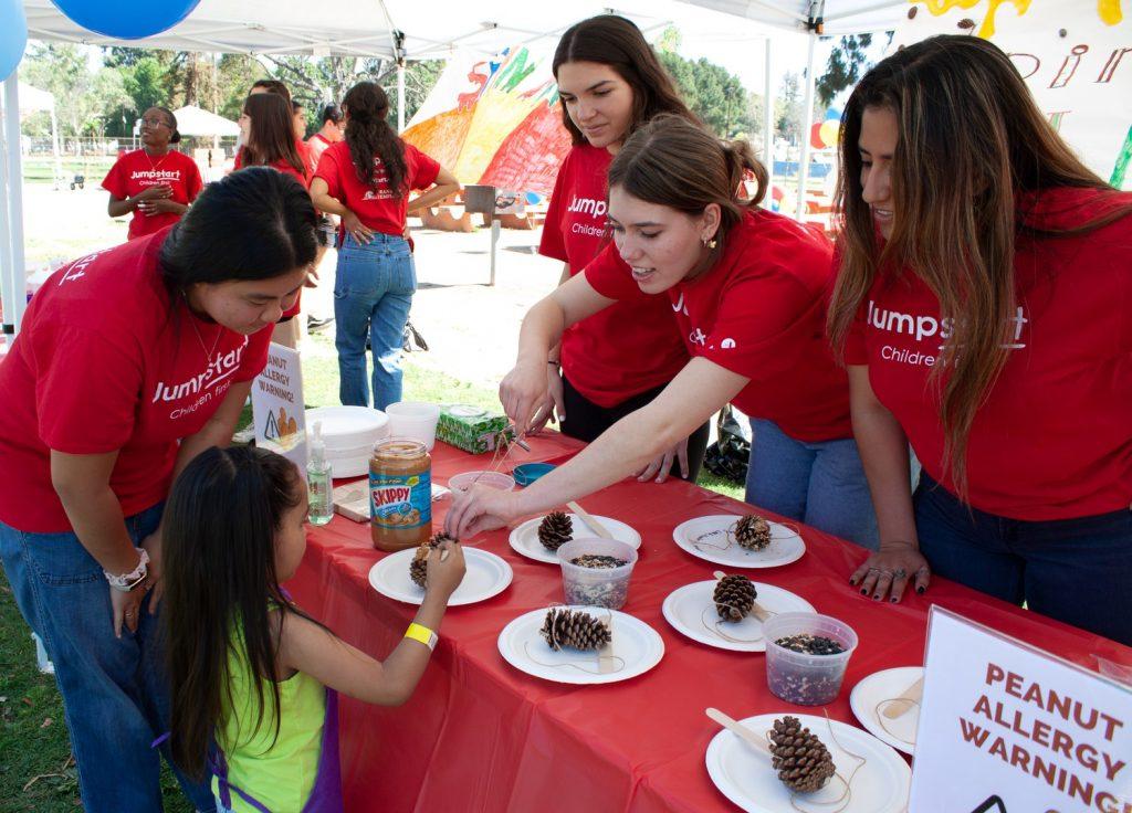 Jumpstart members at the Pine Cone Bird Feeder booth help kids craft a bird feeder using household and outdoor materials. The activity teaches children about the creative ways they can put their surrounding resources to good use.