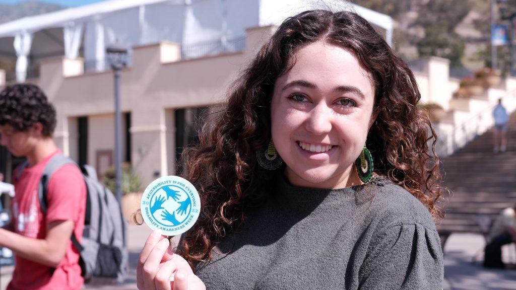 Senior Emily McNutt poses with a promotional sticker from Disability Awareness Week at Pepperdine in March. McNutt became an advocate for accessibility after watching a parent struggle with access during New Student Orientation in fall 2021. Photo courtesy of Emily McNutt