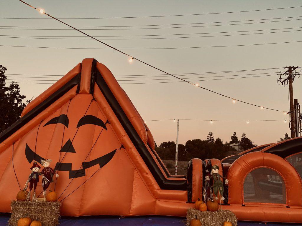 A bright orange, inflatable slide embellishes a jack-o'-lantern face detail and is surrounded by bails of hay, scarecrows and pumpkins at Seasonal Adventures on Oct 3. This patch offered rides and games and sold pumpkins at several locations around Southern California. Photo by Emma Ibarra
