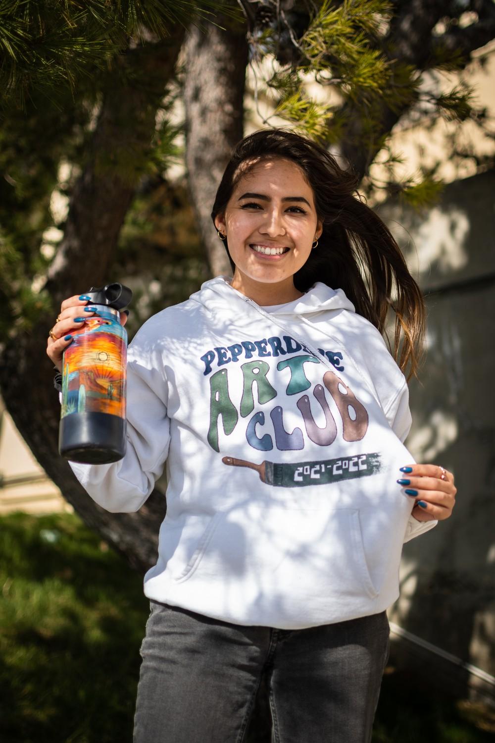 Senior Emily Castillo poses with her painted Hydroflask and art club hoodie. Castillo said art-based social media posts and Bob Ross' paintings inspire her work.