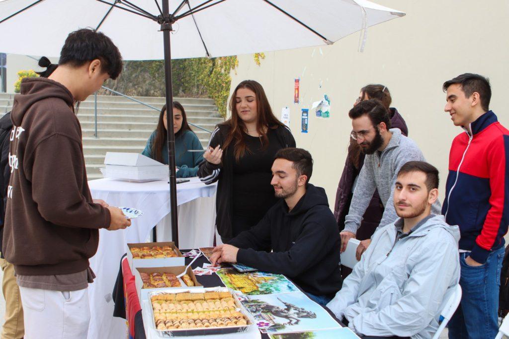 Members of the Armenian Student Association serve baklava to a student at the Global Fest Night Market on March 11. Baklava is a Middle Eastern pastry filled with chopped nuts and drizzled with honey.