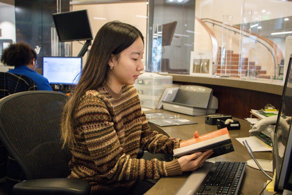 Hannah Gang looks through a book before checking it in at the front desk of Payson Library on Feb. 22. She said she has worked at the library nine hours a week since August 2022.