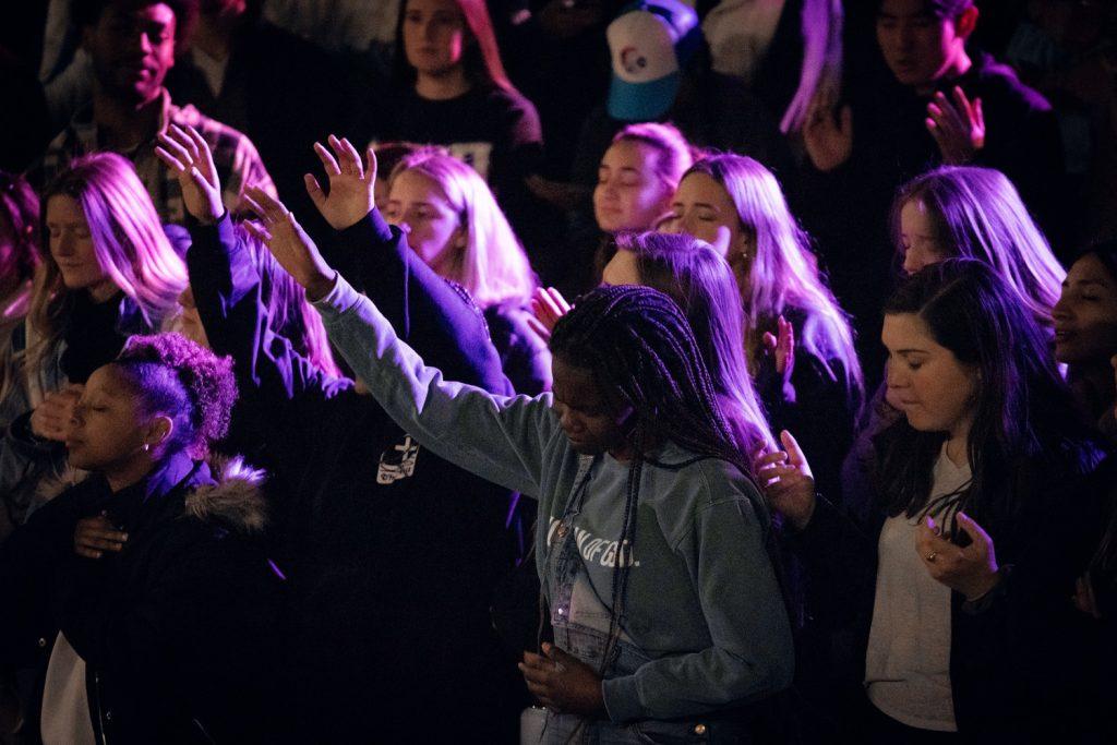 Student raise their hands in prayer during The Well's opening song Feb. 16. The Well usually begins and ends with prayer and worship, with a sermon given in the middle of the service, sophomore Hailey Emmons said.
