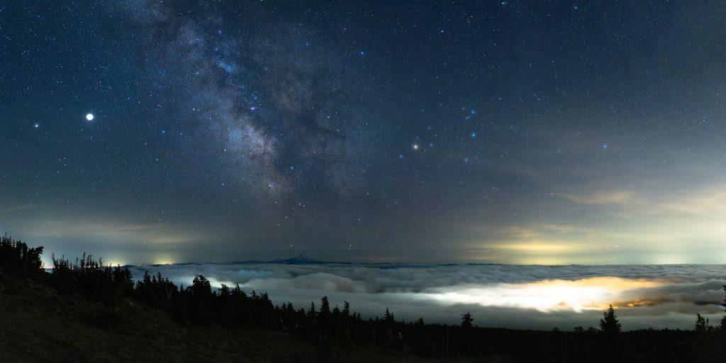 The Milky Way rises above the southern sky from Timberline Lodge, Oregon on July 17, 2020. While Comet NEOWISE was the focus to the west, looking south showed a cloud inversion below us with the lights of Government Camp shining through it, the Milky Way core above Mt. Jefferson, Oregon, and Saturn and Jupiter shining to the left of the core.
