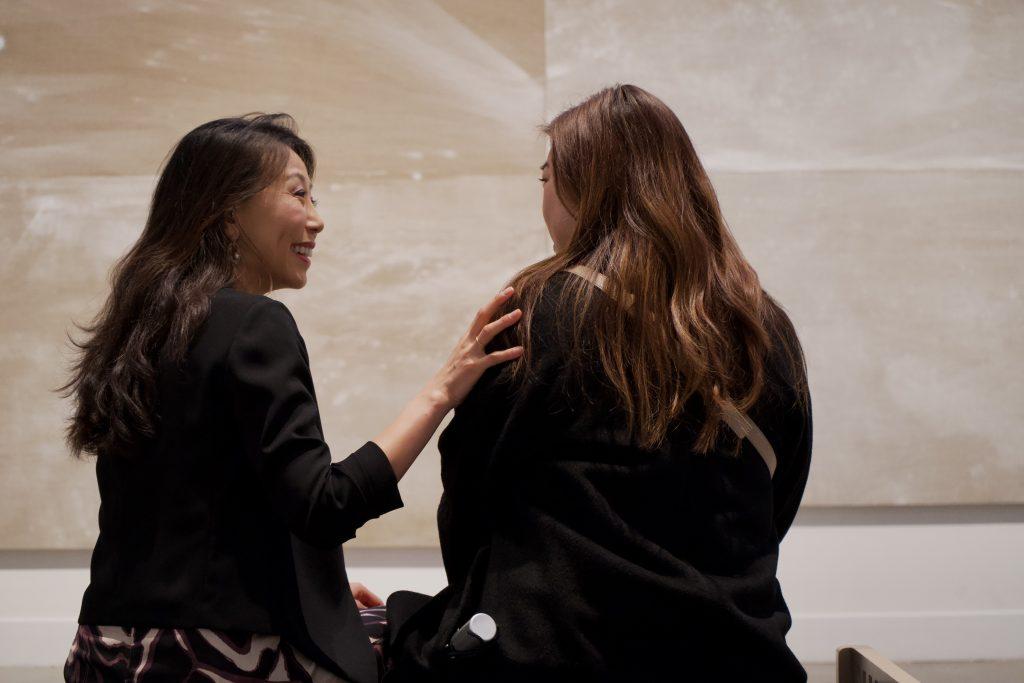 Haejin Fujimura, entrepreneur, lawyer and wife of Makoto Fujimura, converses with an observer in front of "Sea Beyond" on Jan. 20, in the Weisman Museum. The mystifying hues from the painting created the image of a gentle horizon amid a sea of waves.
