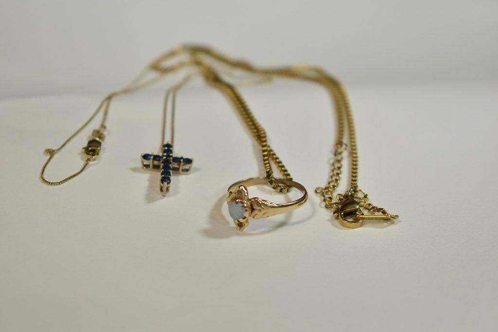 On the left sits the gold cross necklace with the blue stones, and on the right is the gold and opal ring on its chain. These pieces of jewelry have been passed down through generations with love and care. Photo by Mary Elisabeth