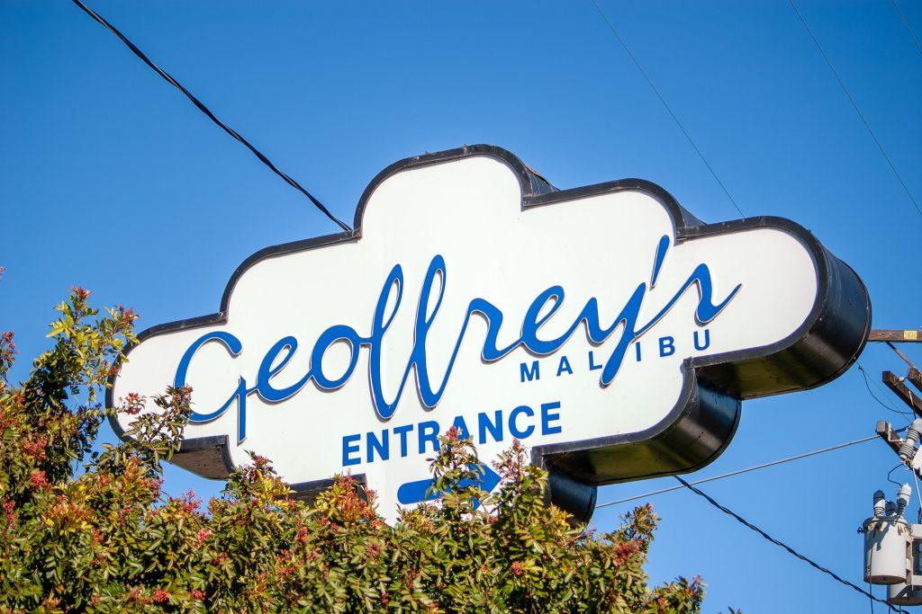 The white and blue sign for Geoffrey's restaurant sits above trees in Malibu on Feb. 11. Established in 1983, Geoffrey’s has served the Malibu community great food for decades according to their website.