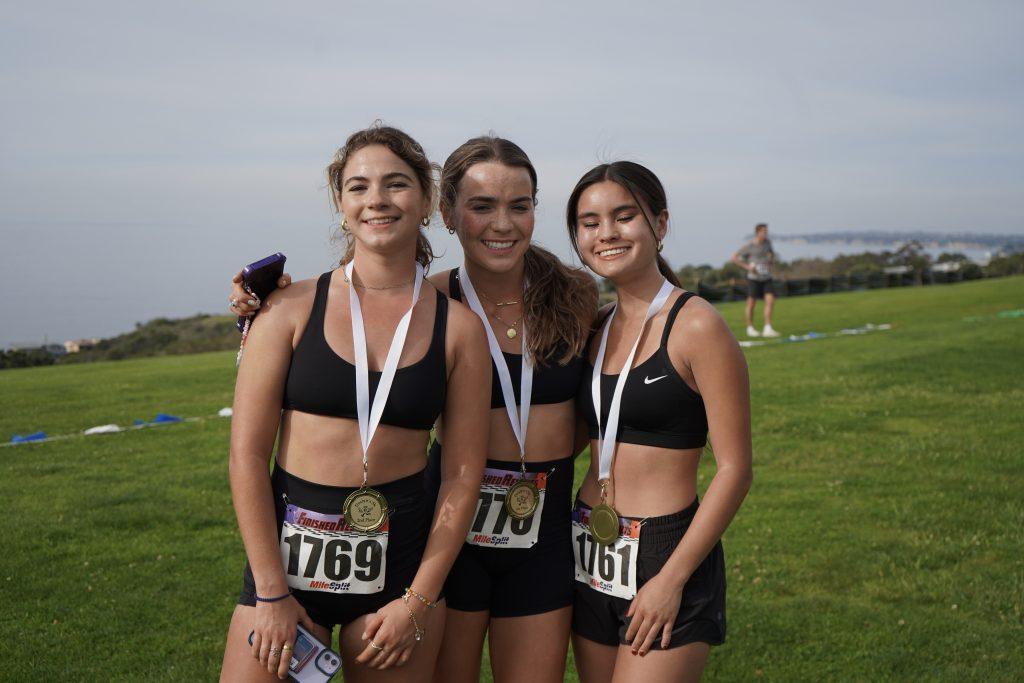 Participants Lacey Reedy, Hannah Bruner and Chloe Connor (left to right) wear white-ribboned medals after completing the 5K March 10, on Lower Alumni Field. Winners included athletes, members of Greek life and other students.