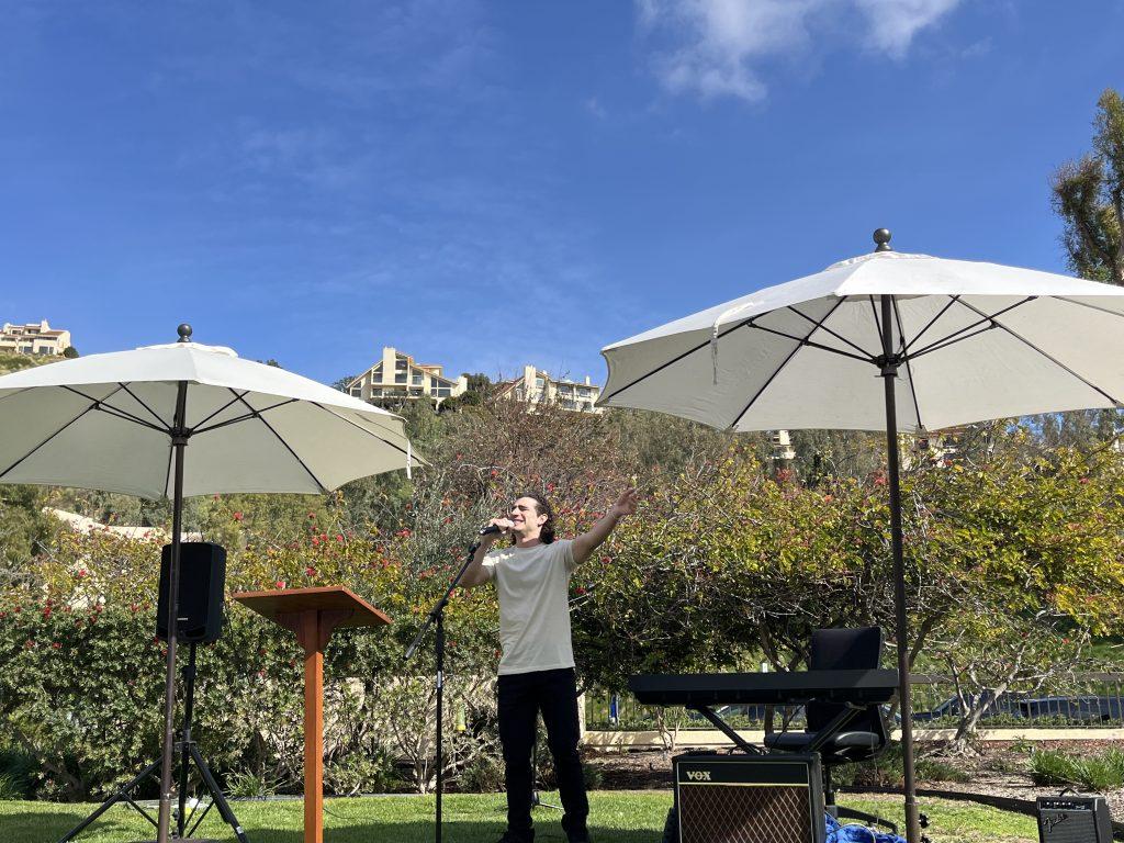 Kash Stepanian encourages the audience to join him in song on the front lawn of the Caruso School of Law on Feb. 14. The audience clapped their hands and sang with him. Photo by Viviana Diaz