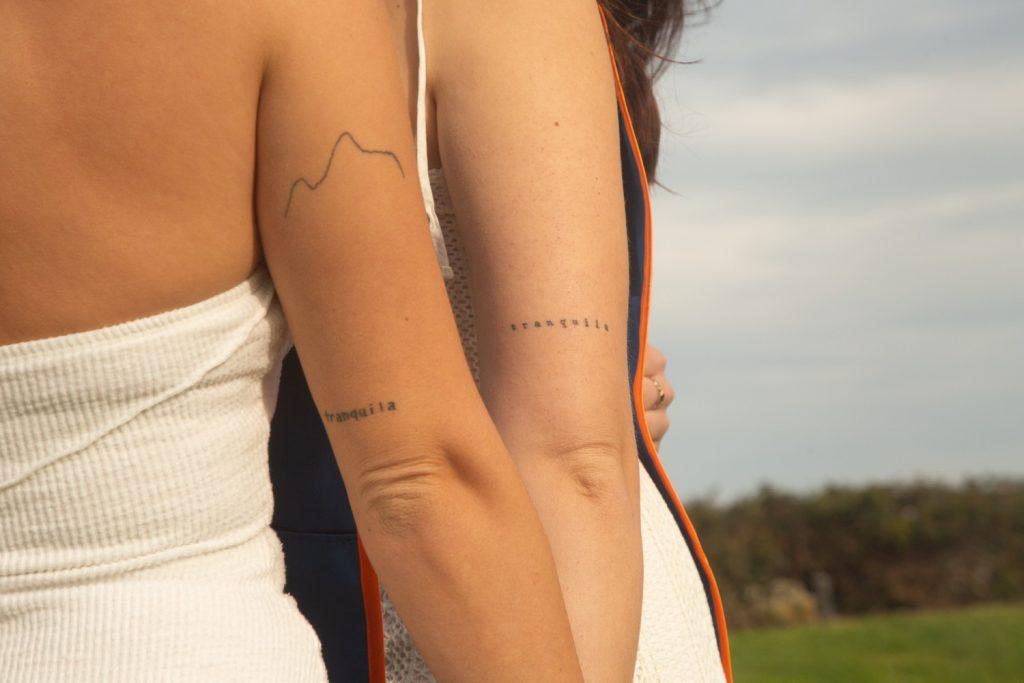 Senior Courtney Wisniewski (left) and her roommate, senior Caroline Pennington (right), show their matching tattoos in their pre-graduation photos at Alumni Park on March 25. Wisniewski said they both have the same tattoo on the backs of their right arms, which reads "tranquila." Photo courtesy of Courtney Wisniewski