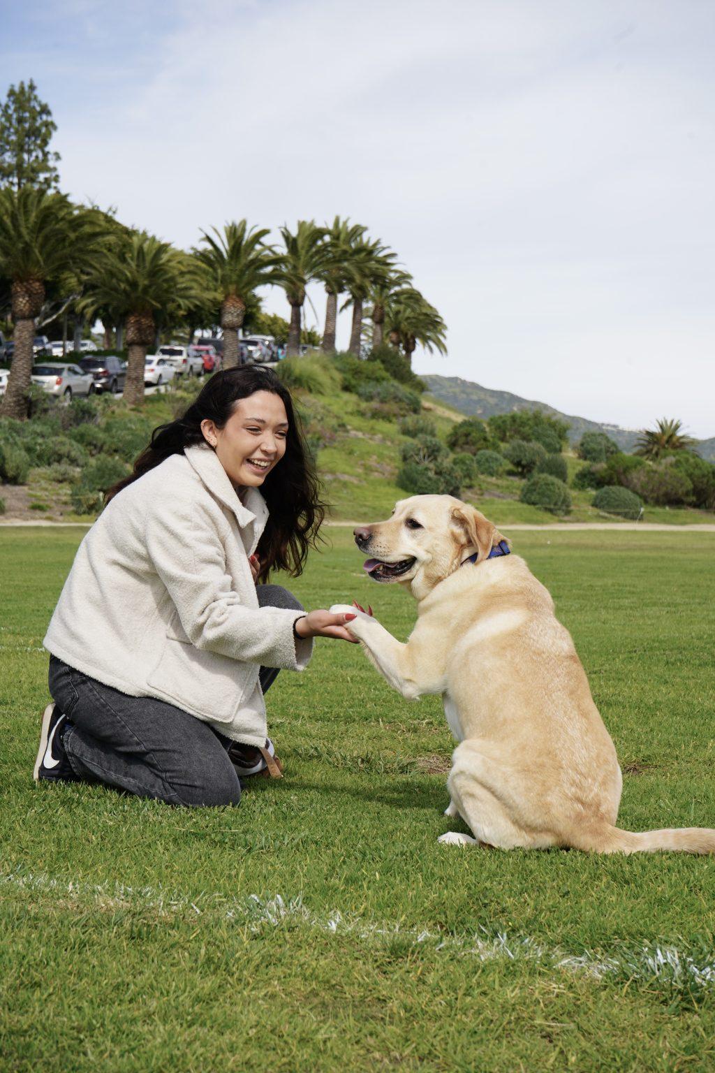 Maria Arguelles smiles and shakes her service dog Nala's paw at Alumni Park on March 25. Arguelles said she and Nala have attended amusement parks and concerts and even traveled on a few planes. Photo by Liam Zieg