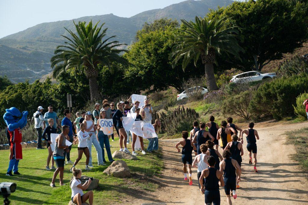 Members of the Men's Cross Country team run past the audience of Waves in attendance for the Waves Invitational on Aug 30, at Alumni Park. Alumni Park features a plethora of curves and hills, something that strikes fear into opponents, Head Coach Lauren Floris said.