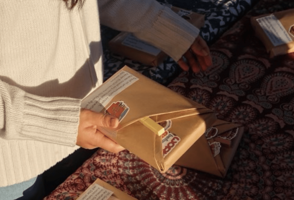 A student holds one of the many wrapped book options that were available at the Oct. 25 event at Upper Mullin Town Square. The package has a description of the book located on the front of the parchment paper and stickers and a highlighter located inside the folds. Photo courtesy of The Board's Instagram page.