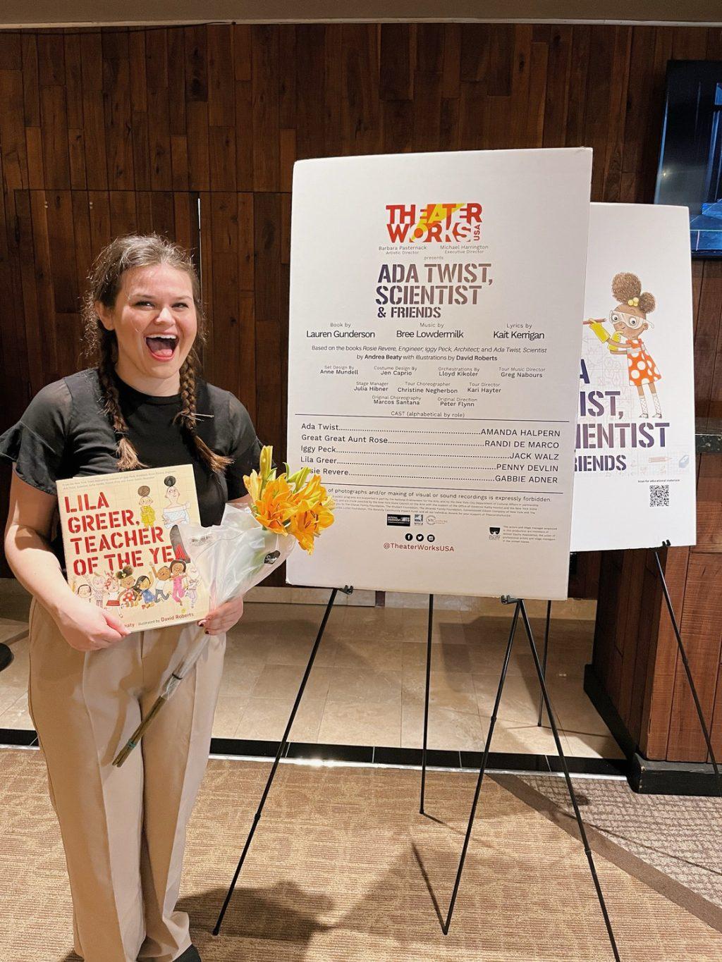 2023 alumna Penny Devlin standing in front of a poster for her current national tour. Devlin said she was grateful to have opportunities after graduation. Photo courtesy of Penny Devlin